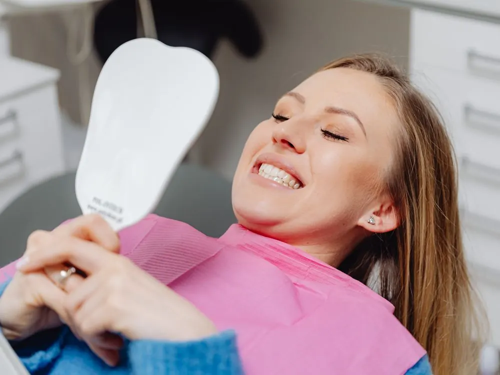 Mulher sorrindo no consultório odontológico olhando o resultado no espelho
